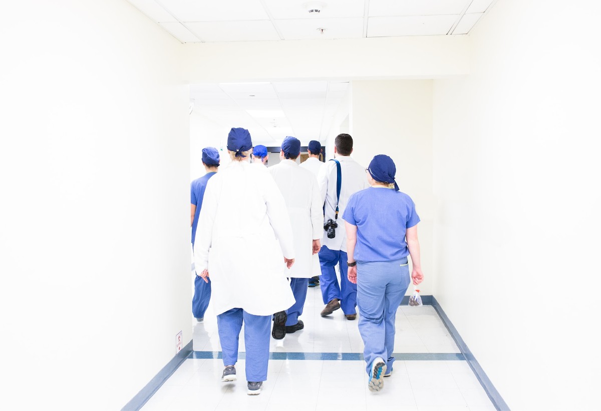 A group of doctors and nurses in blue scrubs walking away from the camera. Photo by Luis Melendez on Unsplaush.