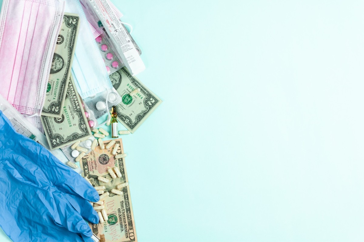 Dollars and healthcare items scattered on a light blue background. Photo by Anastasiia Gudantova.